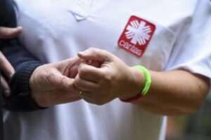 Foto-Ausschnitt auf Brusthöhe: Jemand mit Caritas T-Shirt hält unterstützend die Hand einer Person.